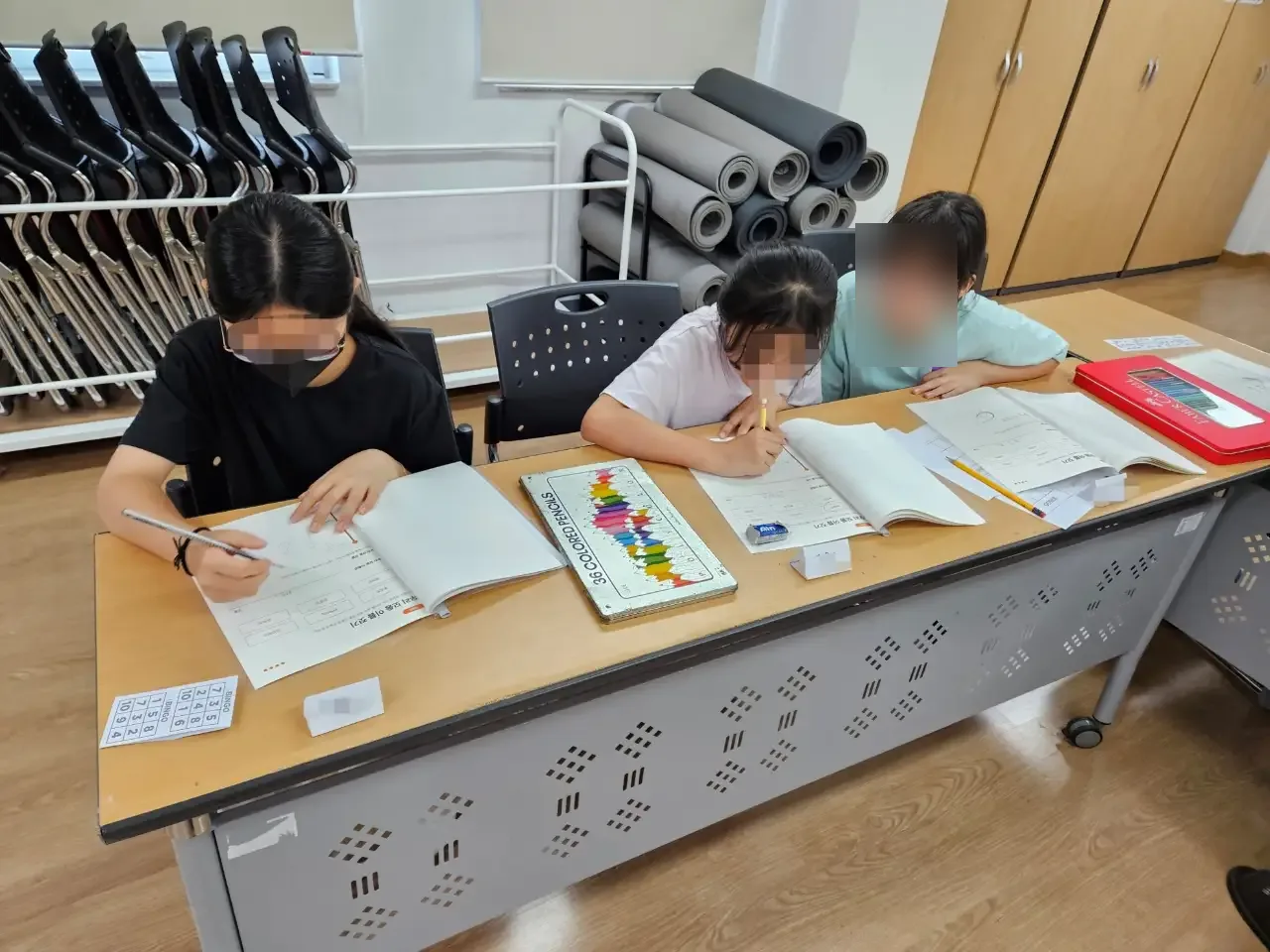책상에 모여 워크북을 펼친 초등학생들 (얼굴 흐림 처리)