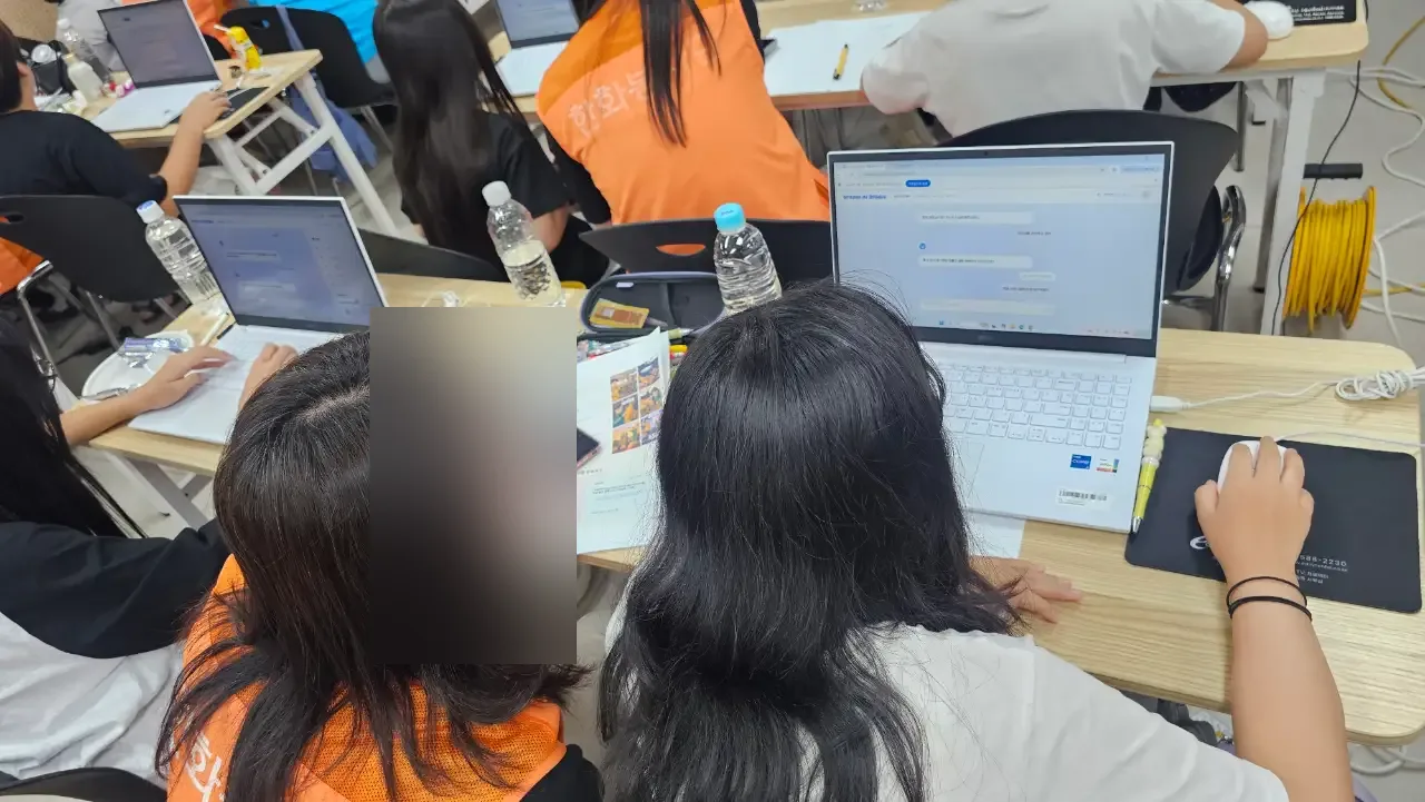 조끼를 입은 봉사자와 학생들이 노트북 앞에 앉은 뒷모습