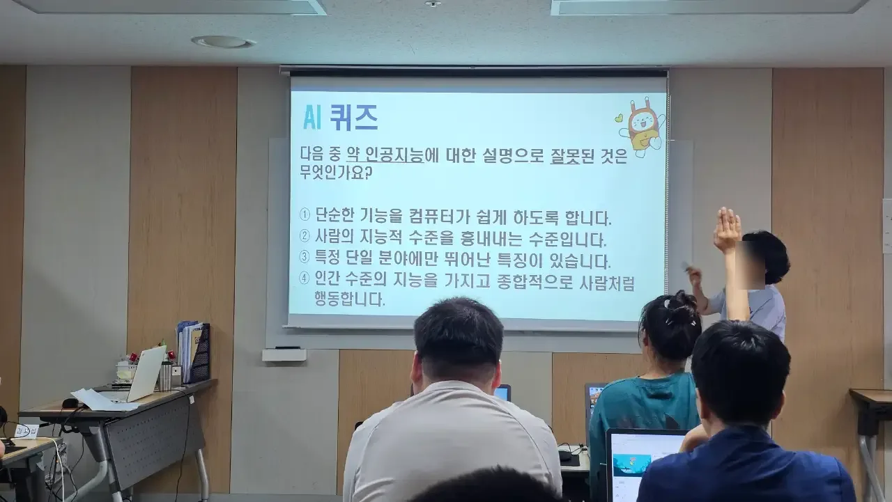 스크린의 AI 퀴즈를 보며 손을 든 수강생들 (얼굴 흐림 처리)
