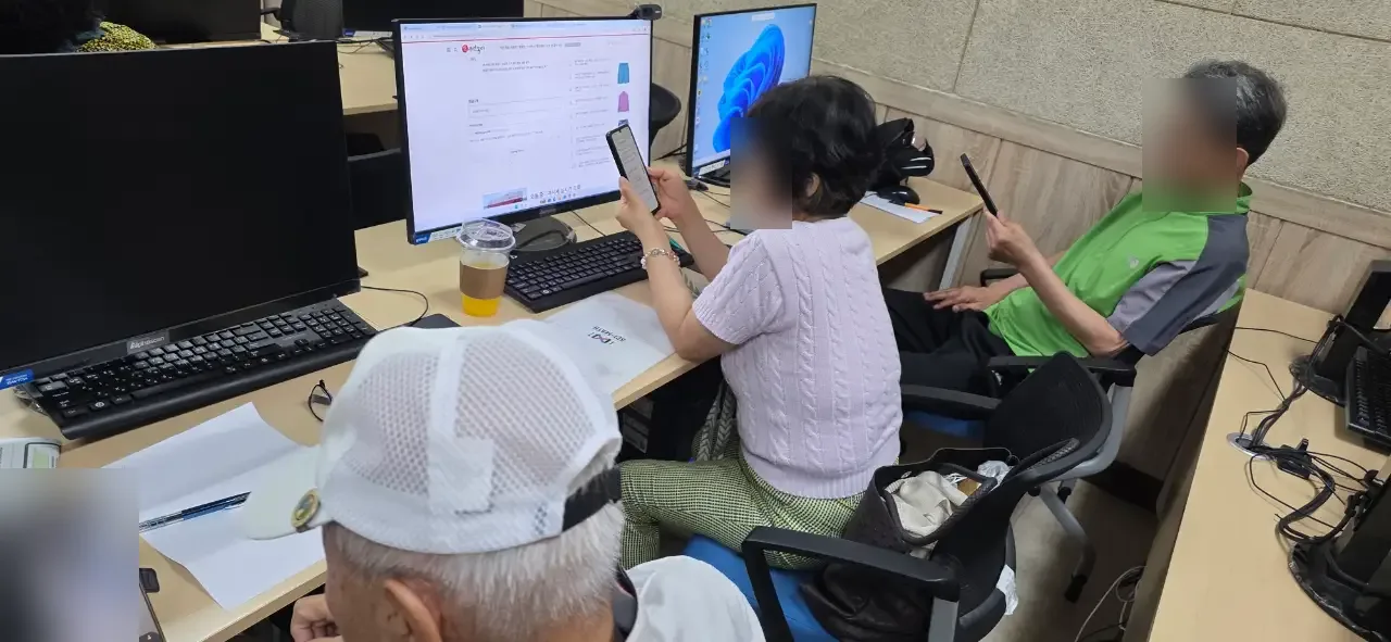 모니터 앞에서 스마트폰을 든 시니어 수강생 (얼굴 흐림 처리)